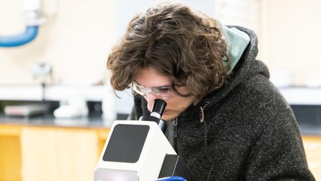 A student looks into a microscope in a science lab setting