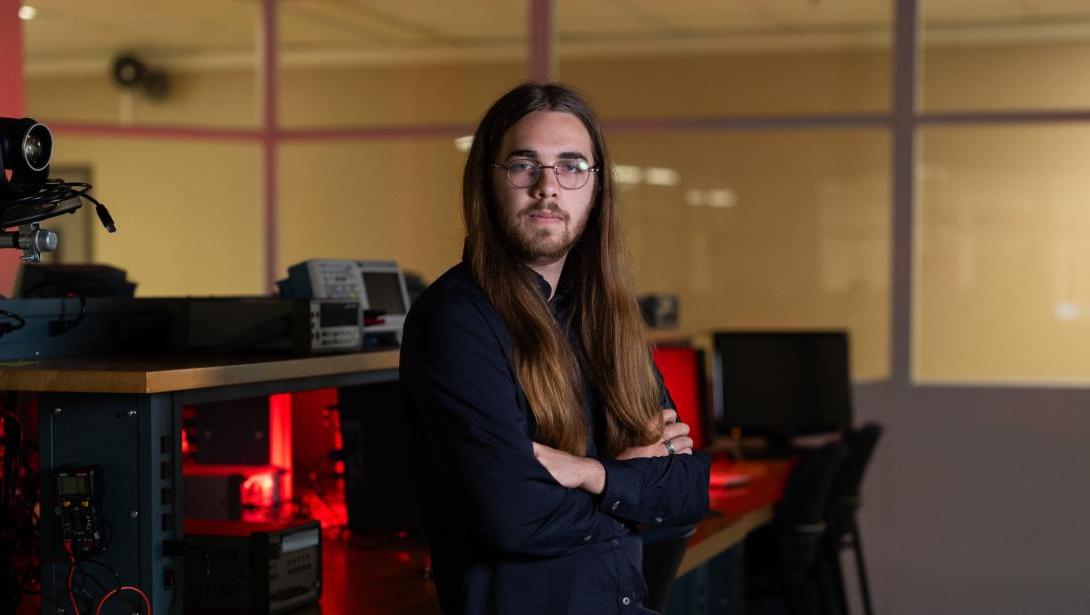 An individual in business attire stands with arms crossed in a classroom